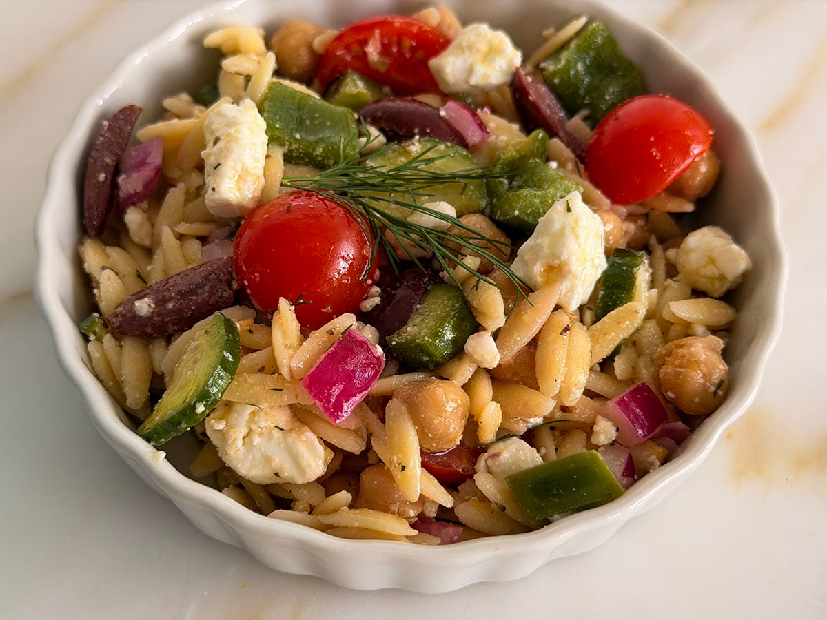 Greek orzo pasta salad in a white bowl with dill on top