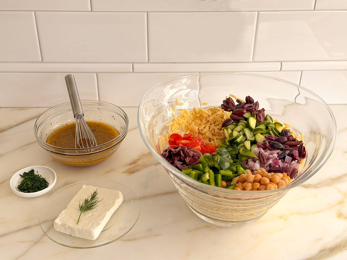 A glass bowl filled with ingredients for pasta salad