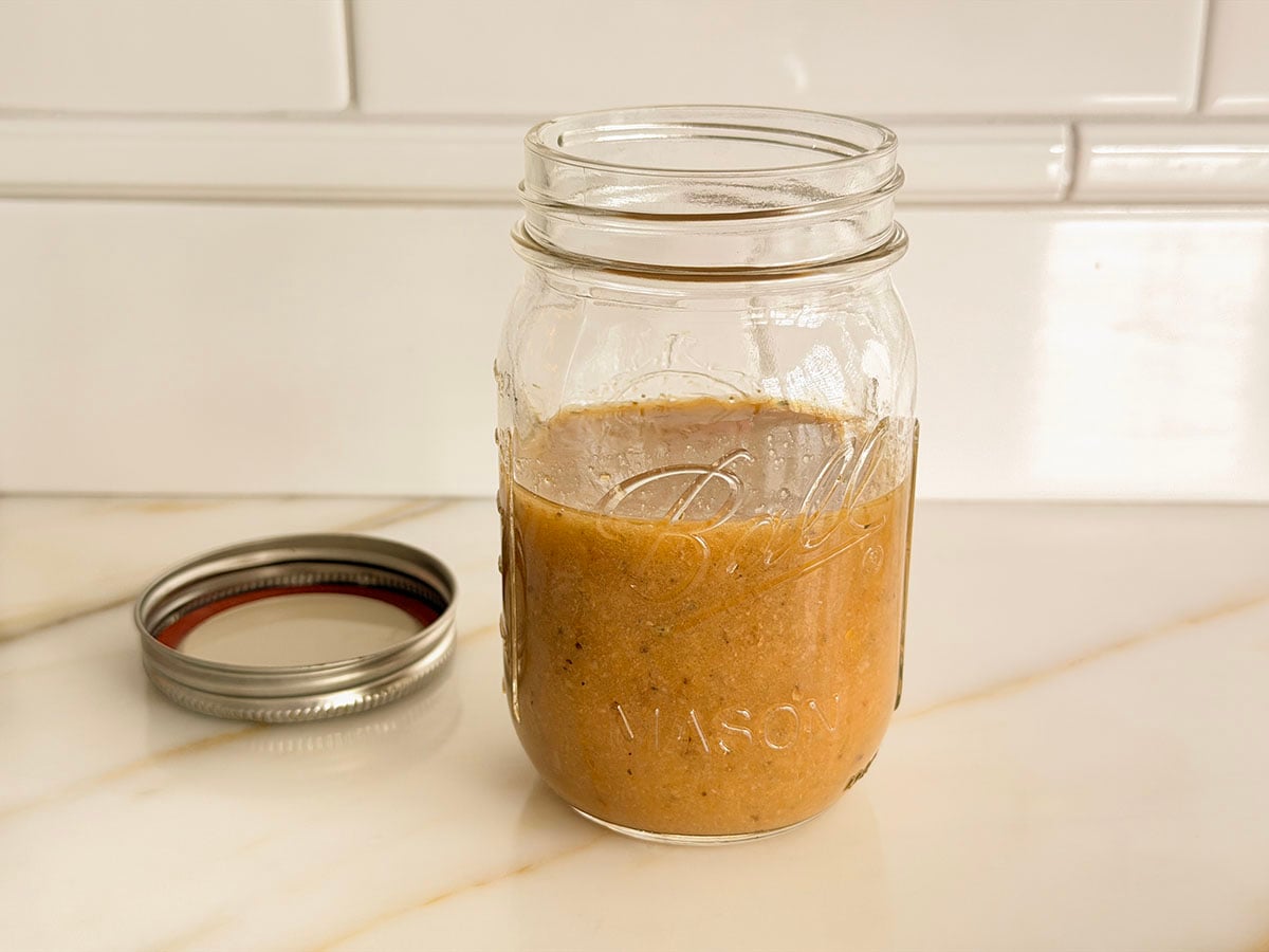 Jar containing Greek salad dressing with the lid off to the side