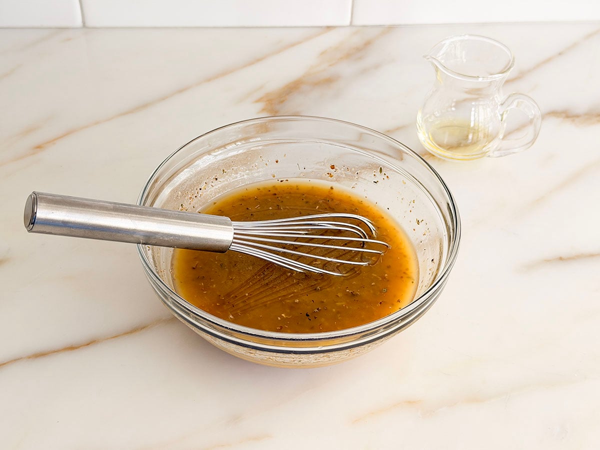 Greek salad dressing in a glass bowl with a small whisk in it