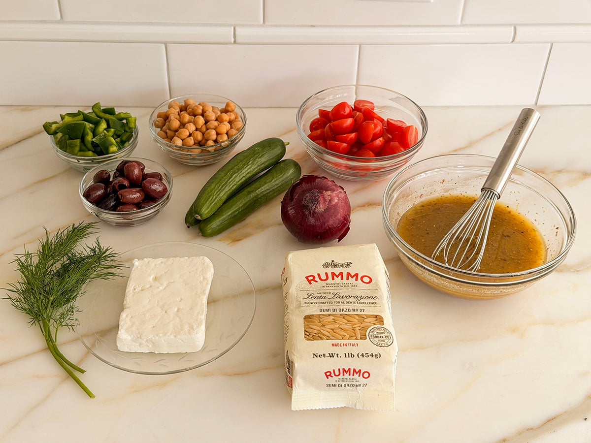 Ingredients for Greek orzo pasta salad on a marble countertop