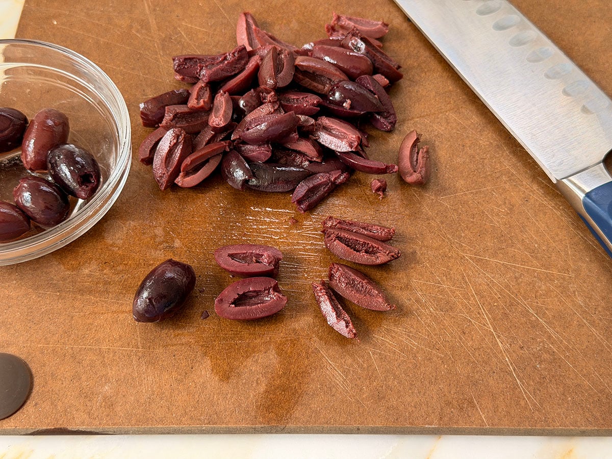 Kalamata olives on a tan cutting board with knife on the side