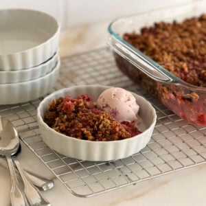 Rhubarb crisp with a scoop of ice cream in a white dish with spoons on the side