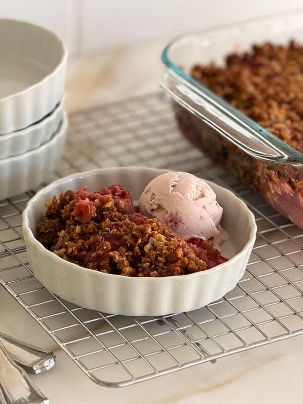 Rhubarb crisp with a scoop of ice cream in a white dish with spoons on the side