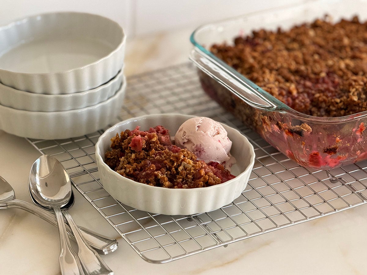 Rhubarb crisp with a scoop of ice cream in a white dish with spoons on the side