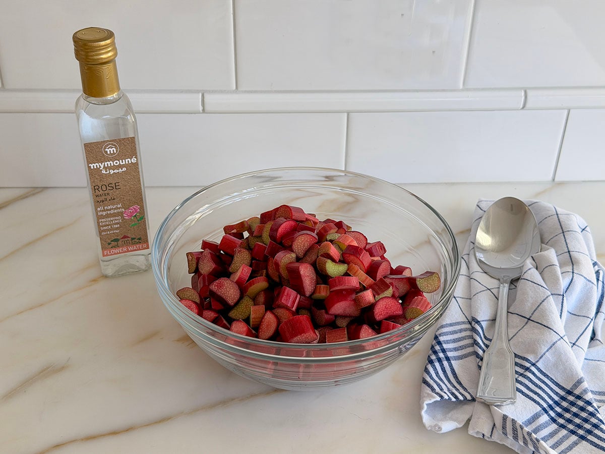 Rhubarb diced in a glass bowl with a bottle of rose water on the side