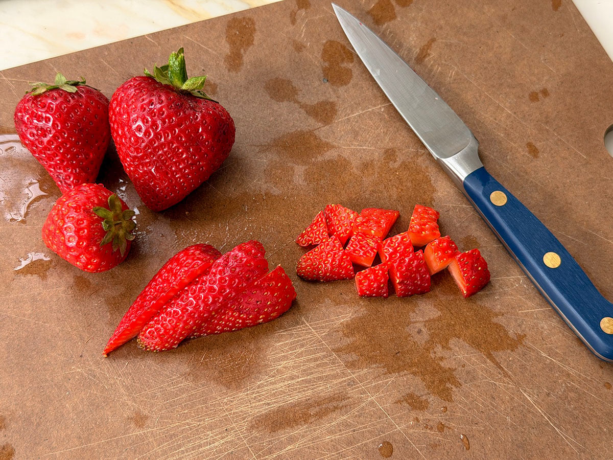 Strawberries diced on a cutting board with a knife with a blue handle