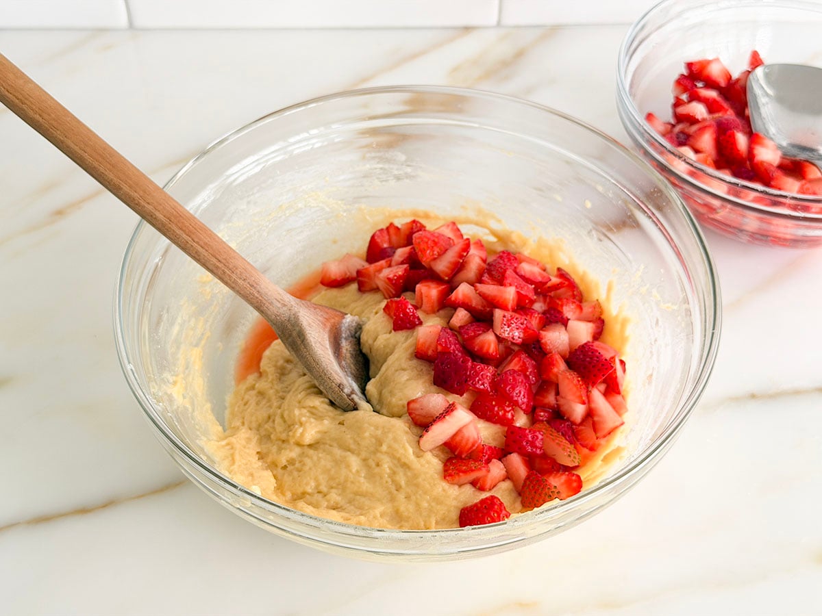 Strawberries mixing into muffin batter with a wooden spoon