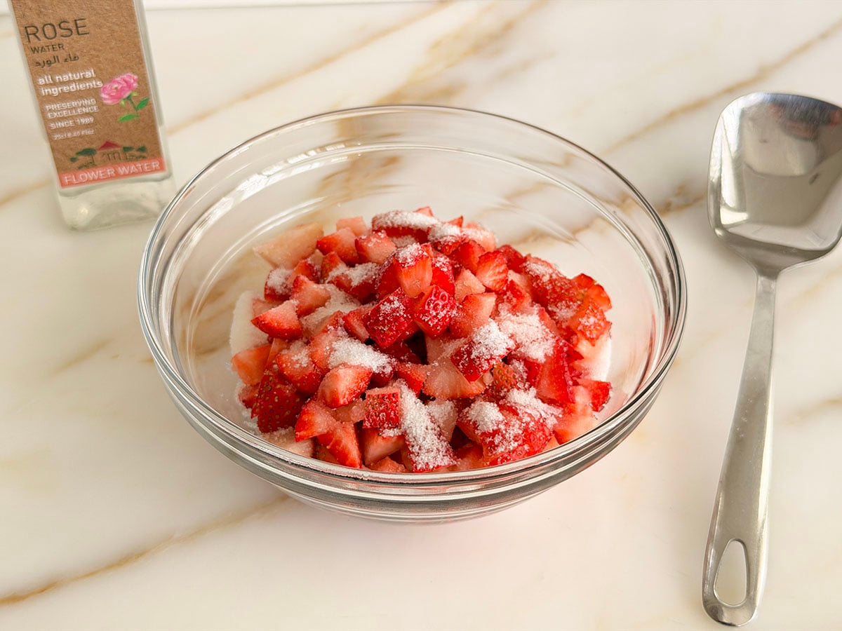 Diced strawberries in a glass bowl with granulated white sugar on top
