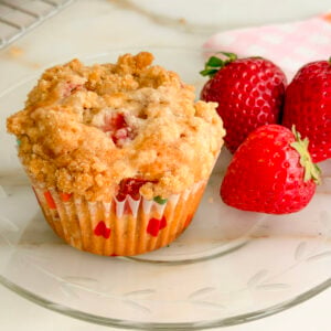Strawberry muffin on a glass plate with three strawberries and a pink napkin on the side