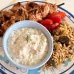 Tzatziki sauce in a blue bowl with kebabs on the side