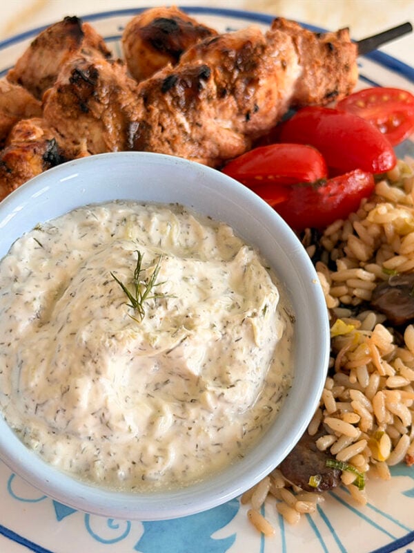 Tzatziki sauce in a blue bowl with kebabs on the side