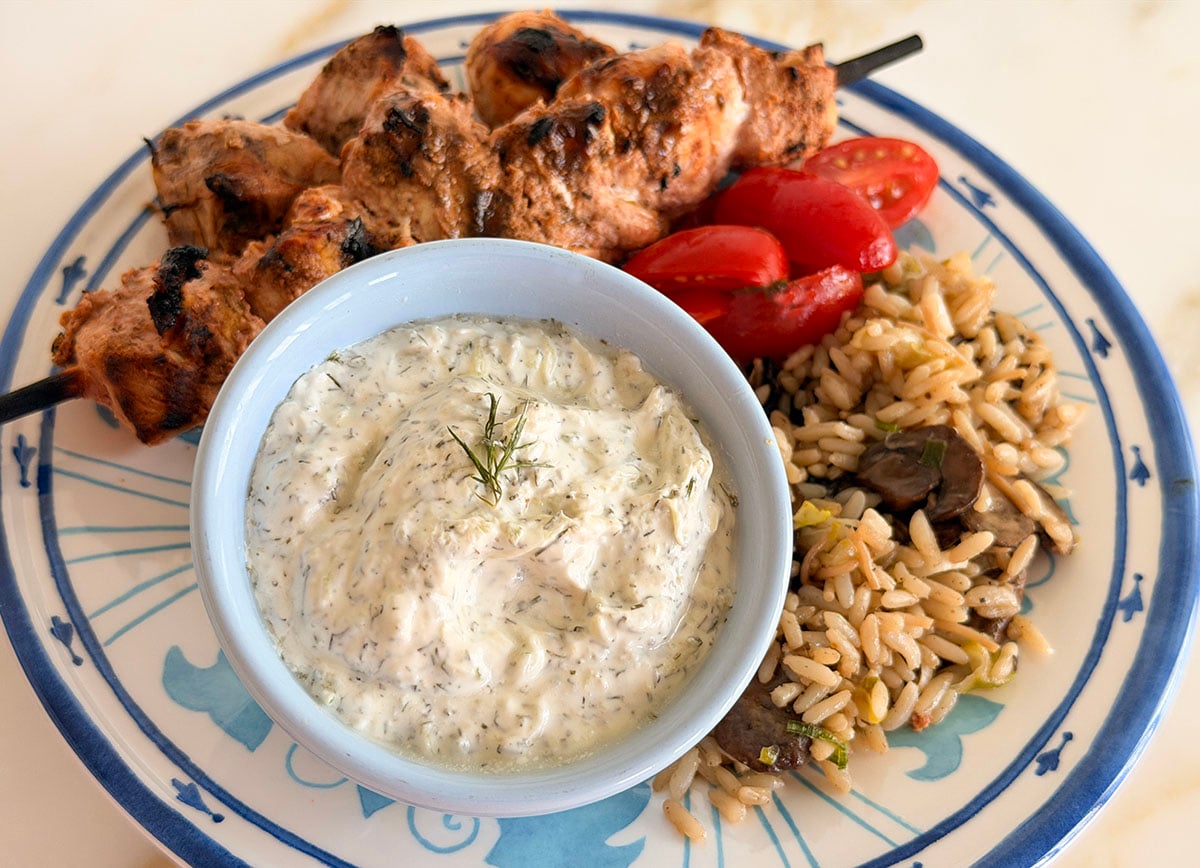 Tzatziki sauce in a blue bowl with kebabs on the side