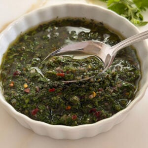 Chimichurri sauce in a white dish with a spoon lifted out of it