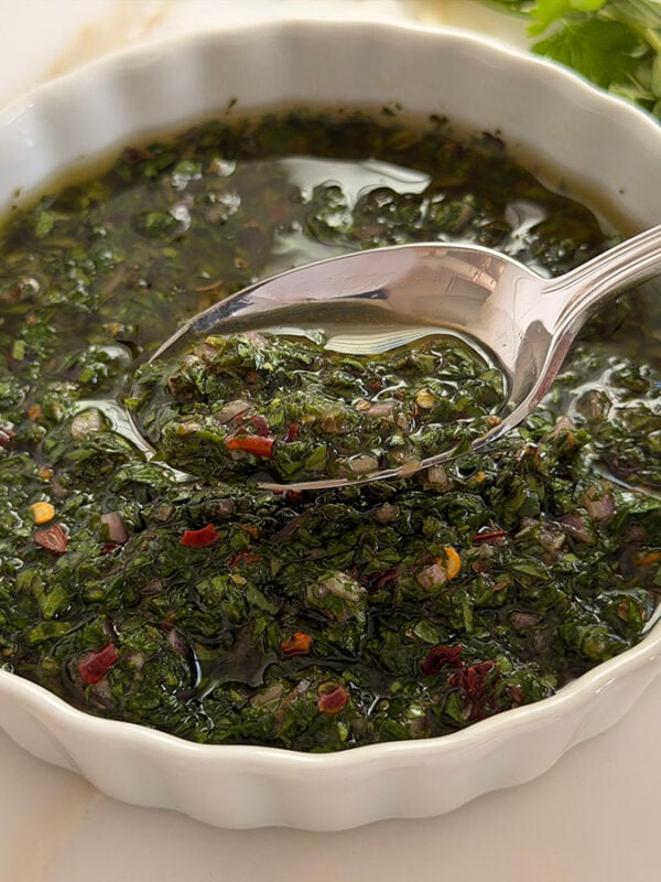 Chimichurri sauce in a white dish with a spoon lifted out of it