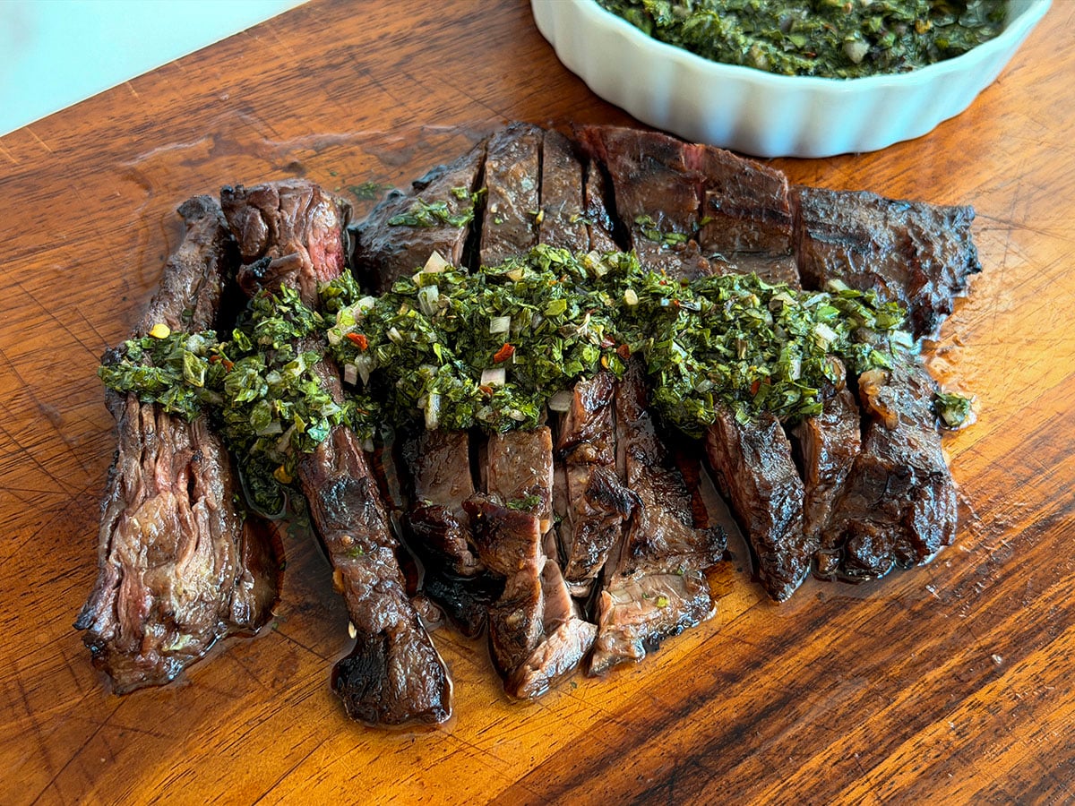 Chimichurri sauce spooned over grilled steak on a wood cutting board