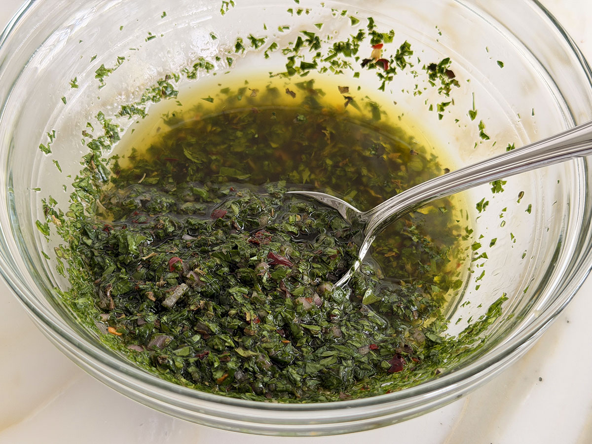 Chimichurri sauce in a glass bowl with a spoon in it