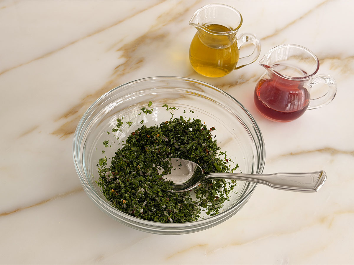ingredients for chimichurri stirred together in a glass bowl