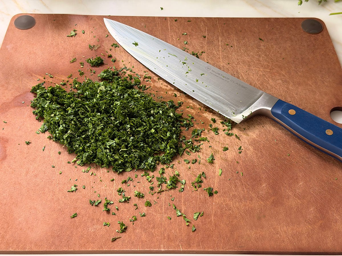 Chopped parsley and oregano on a cutting board with knife on the side