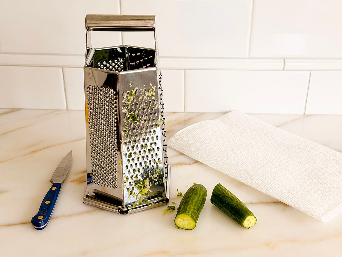 A metal box grater with cucumbers on the side