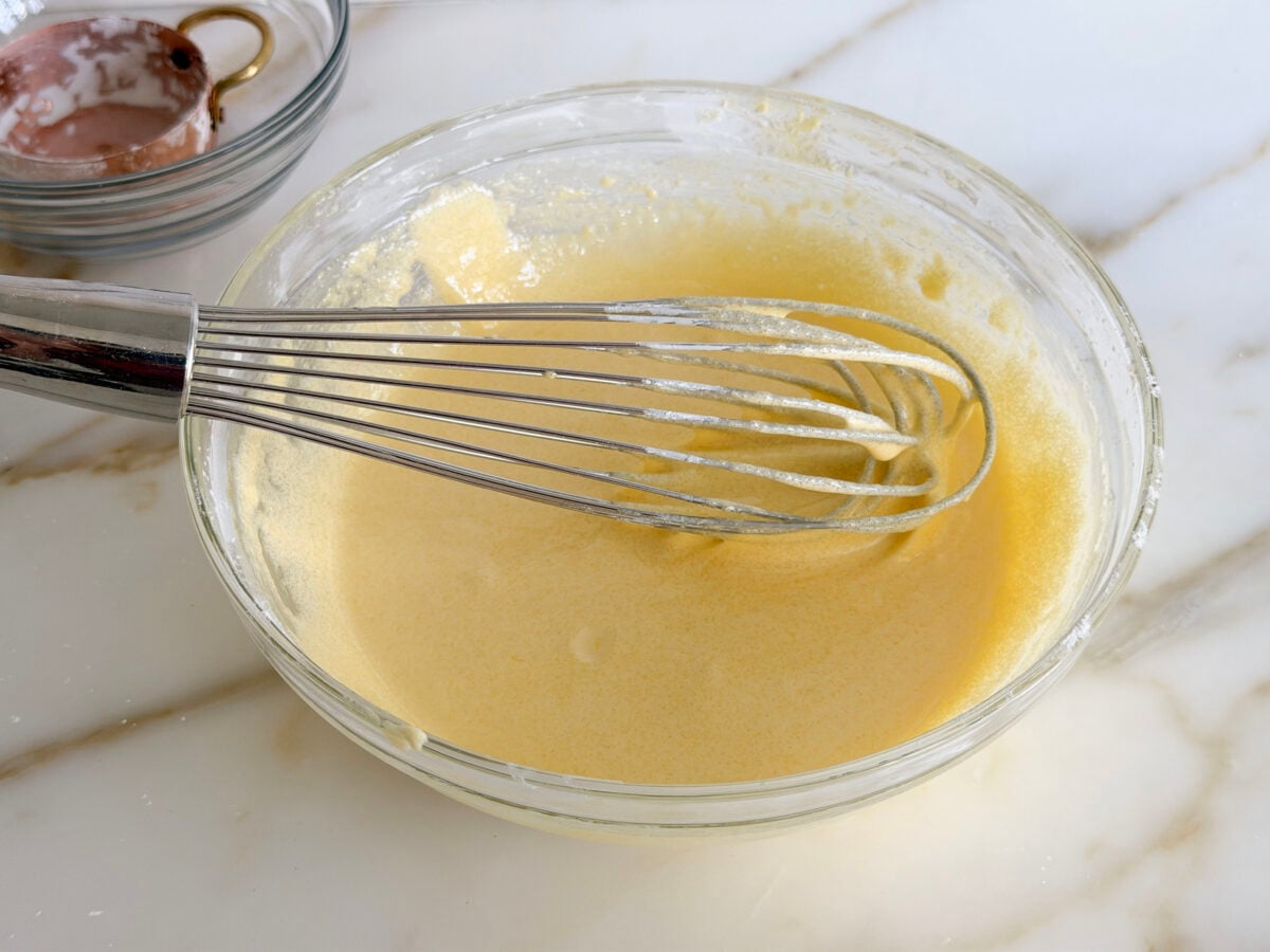 Yellow egg yolk mixture with a whisk in a glass bowl