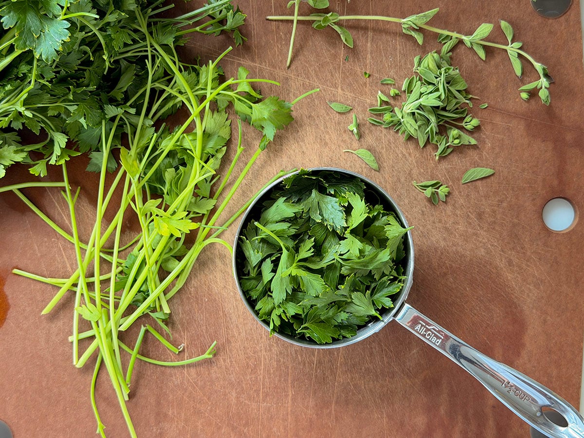 Parsley leaves in a measuring cup on a cutting board