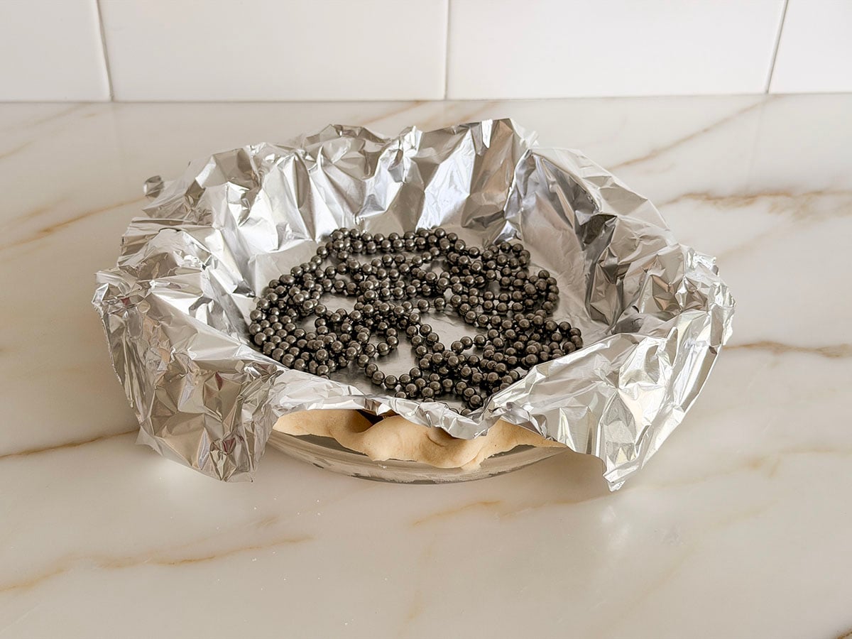 Pie crust in a pie plate covered with aluminum foil and filled with pie weights